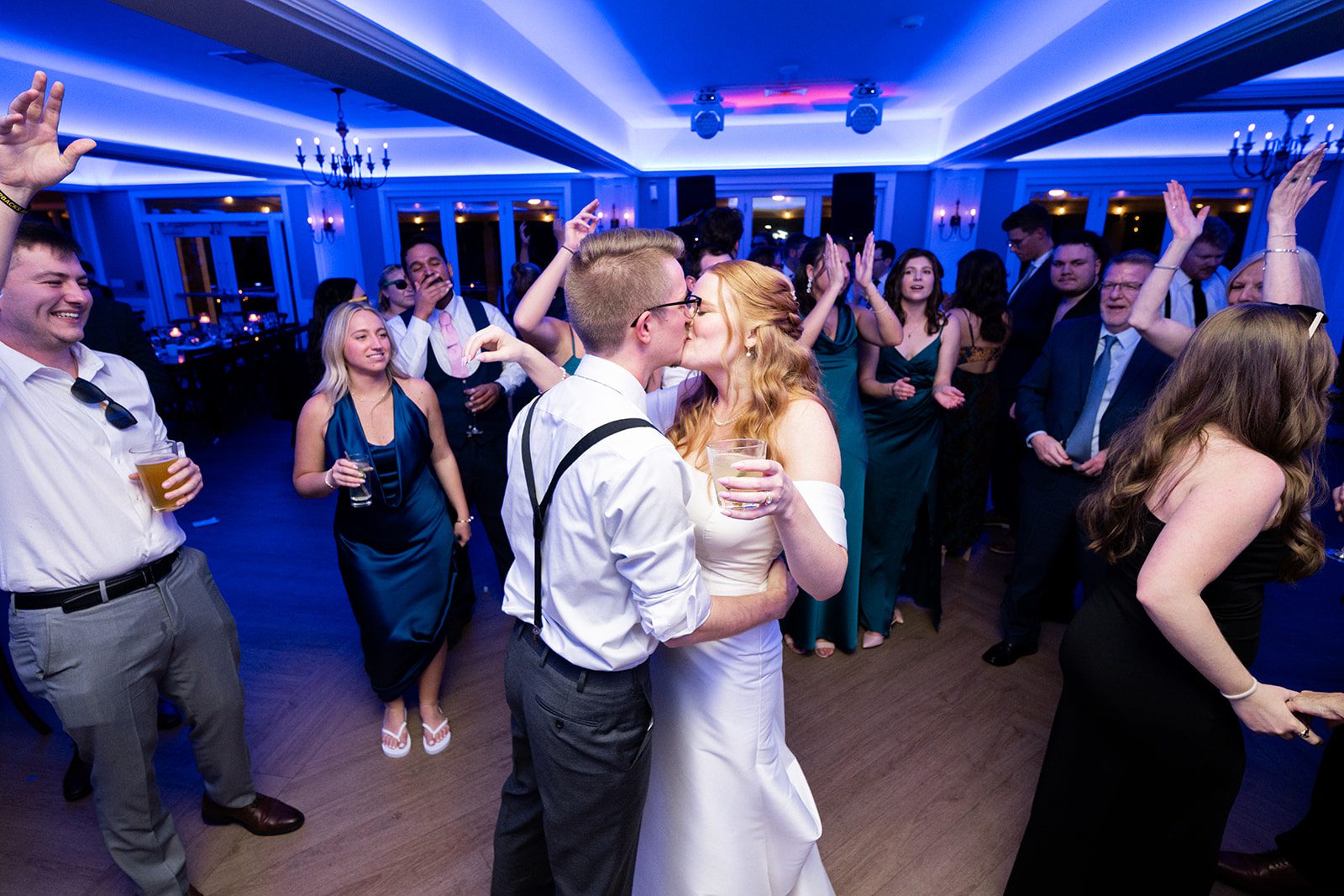 Wide view of the couple and guests dancing under purple and blue lights.