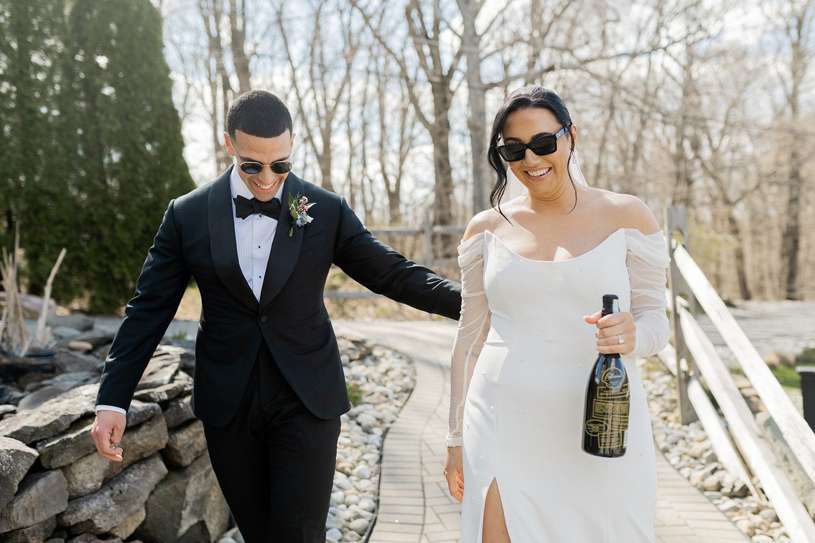 Ashley and Monte walk together in sunglasses while carrying champagne.