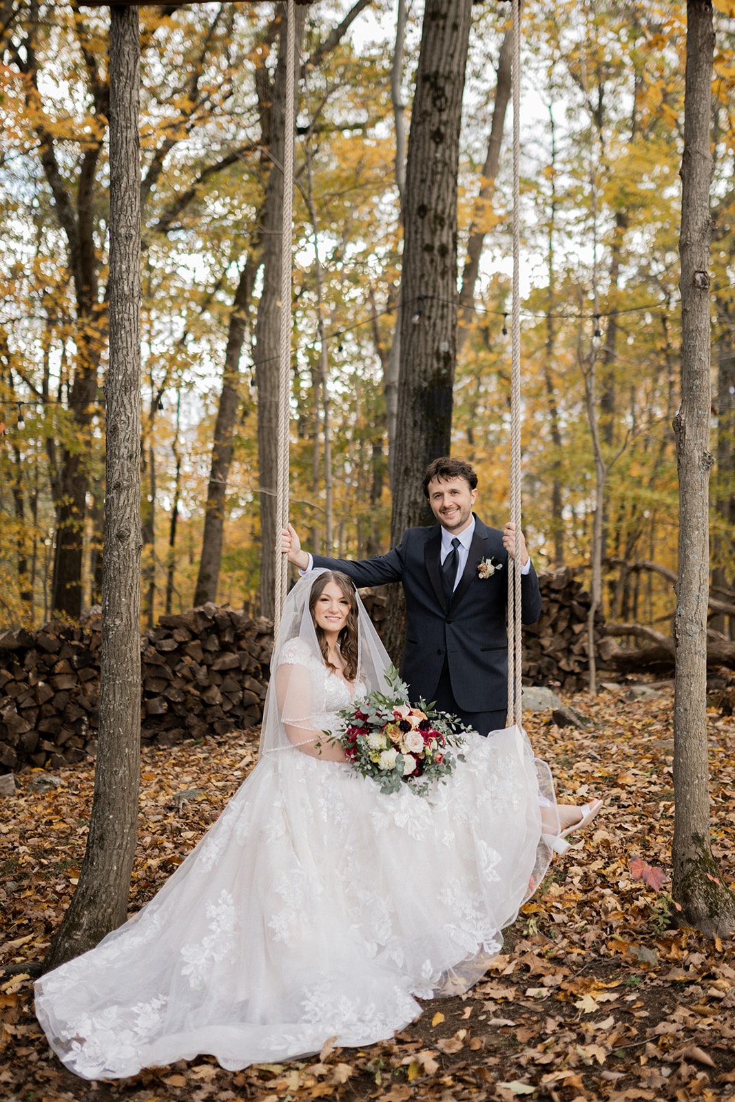 Alexis and Christian pose in the forest with fallen leaves around her dress.